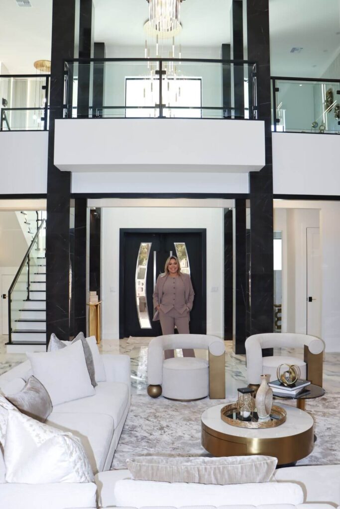 Luxury double-height great room in custom Lady Lake Florida residence featuring black marble columns, contemporary furnishings, glass railings, and dramatic architectural volume.