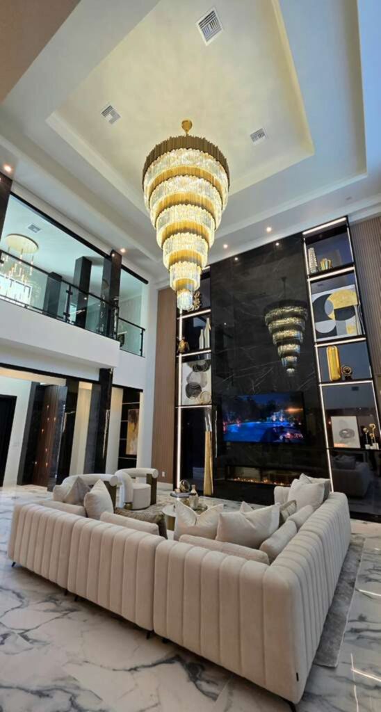 Completed double-height great room designed by Zamira Ariza featuring a custom marble fireplace, crystal chandelier, contemporary furnishings, and architectural lighting in Flaava House.